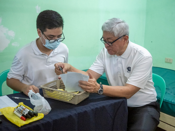 Tzu Chi International Medical Association (TIMA) co-founding member Dr. Josefino “Jo” Qua (right) checks on the prescribed medicines prepared by medical student volunteer Vince Enrico Canda Vitug. 