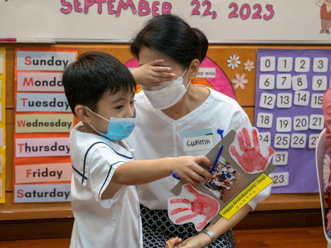 Student covers her grandmother’s eyes to surprise her with a customized greeting card on Grandparents Day. 【Photo by Matt Serrano】