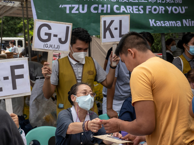 Volunteers hold up signs with the first letter of beneficiaries’ surnames, making the process of claiming goods fast and smooth. 【Photo by Matt Serrano】