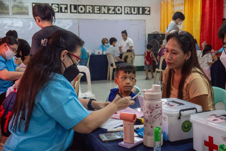 Dr. Tem de los Santos prepares a prescription for Mark Joseph Gutual (center), son of Aiza dela Vega (right).