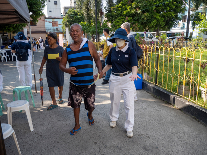 A Person With Disability is guided into the medical mission waiting area by a Tzu Chi volunteer.