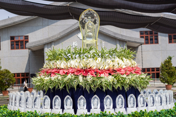 Crystal Buddhas laid out in tables are adorned with fresh flowers and lush greens. 【Photo by Matt Serrano】