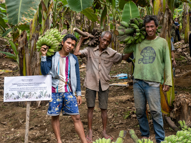 Eric Parcon (leftmost), Armando Dusonan Jr. (rightmost), and Armando Dusonan Jr.'s father (center) pose for a shot with their banana harvest. 【Photo by Matt Serrano】