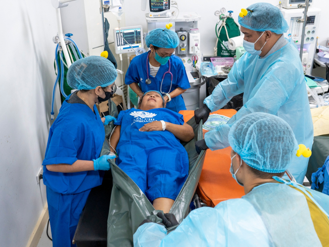 Volunteers work together to transfer Myrna Tanuhay to the operating table. 【Photo by Harold Alzaga】