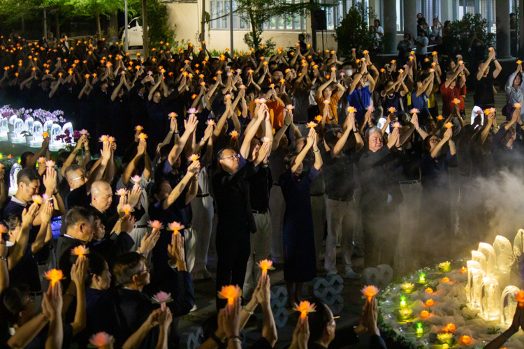 The ceremony concludes as attendees lift their lotus candles while singing a prayer for peace in the world.