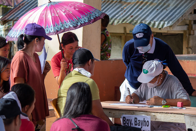 A resident from Brgy. Bayho provides shade to a Tzu Chi volunteer with an umbrella during stub distribution. 【Photo by Matt Serrano】