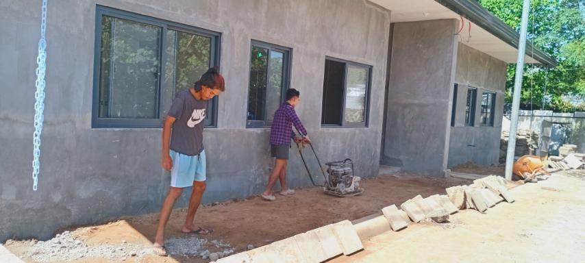 Beneficiaries use a compactor machine to level and smooth the ground before cementing. 