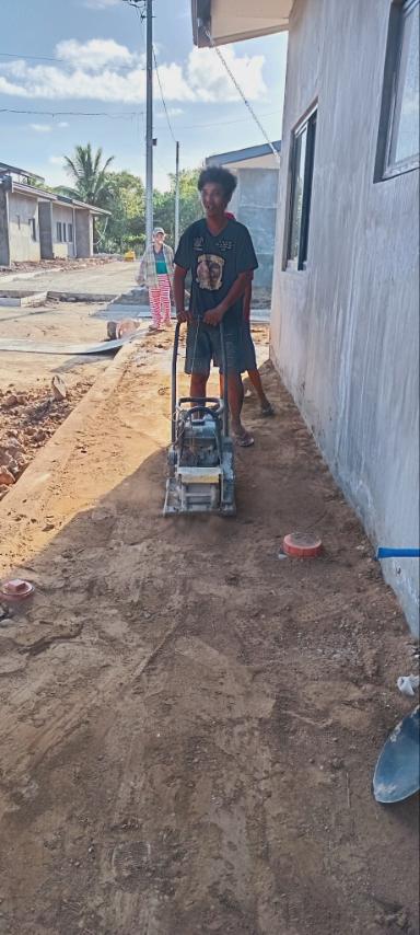 Beneficiaries use a compactor machine to level and smooth the ground before cementing. 