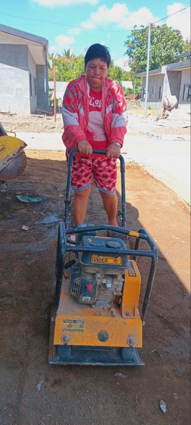 Beneficiaries use a compactor machine to level and smooth the ground before cementing. 