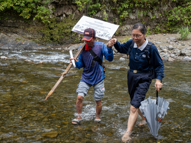 A farmer assists a Tzu Chi volunteer in crossing the river on their journey to the banana planting site. 【Photo by Matt Serrano】